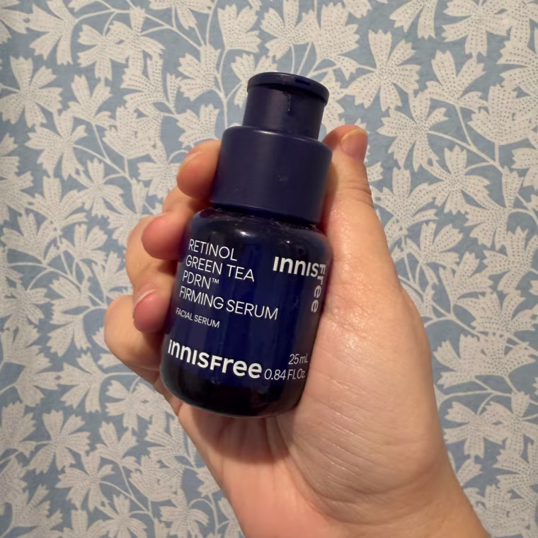 Hand holding theInnisfree Retinol Firming Serum against blue and white flowered wallpaper.