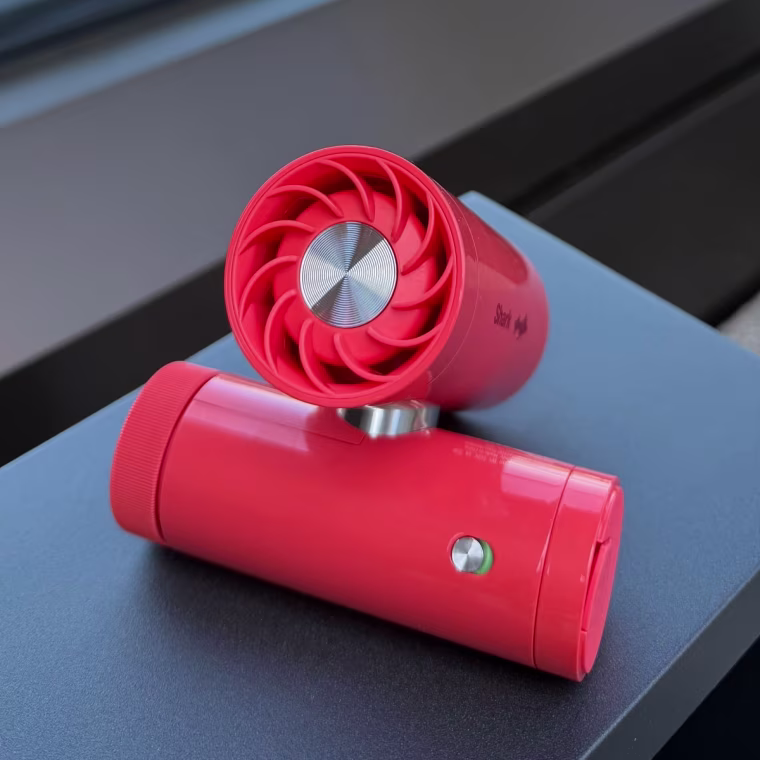 Red mini fan on a table with the city in the background.