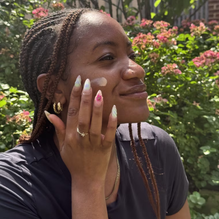 A woman applying Tatcha’s The Silk Sunscreen on her cheek while outside.