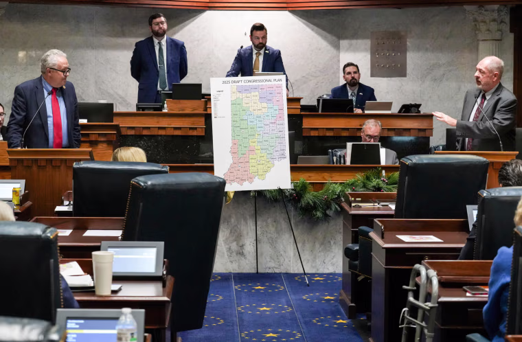 People sit inside of a senate chamber around a poster of a congressional map