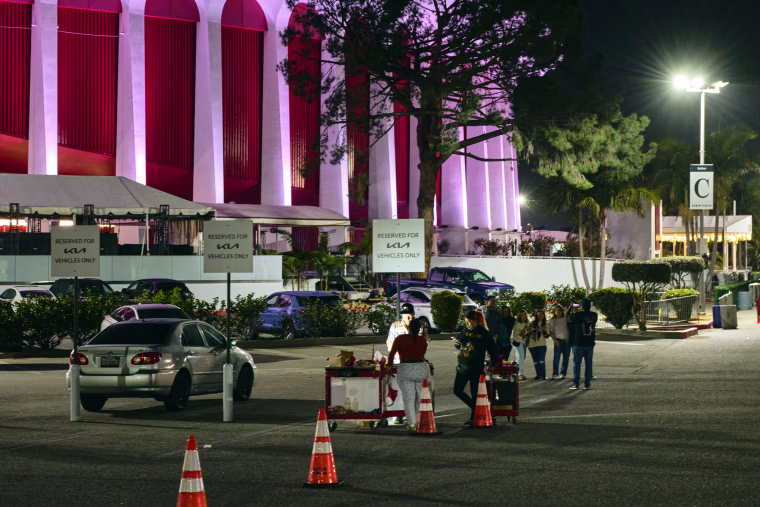 People stand near vendor carts in a parking lot outside of the Kia Forum building