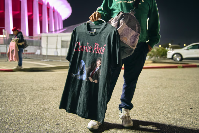 A person holds a Charlie Puth t-shirt in a parking lot