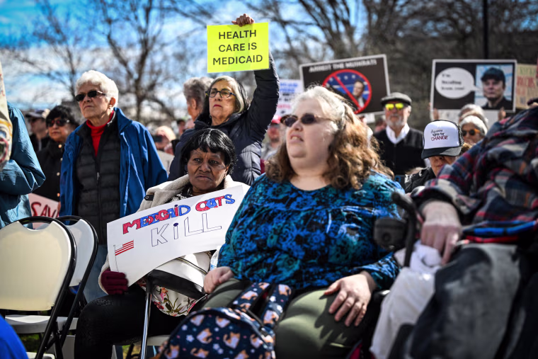 A large crowd of people hold signs against medicaid cuts outside