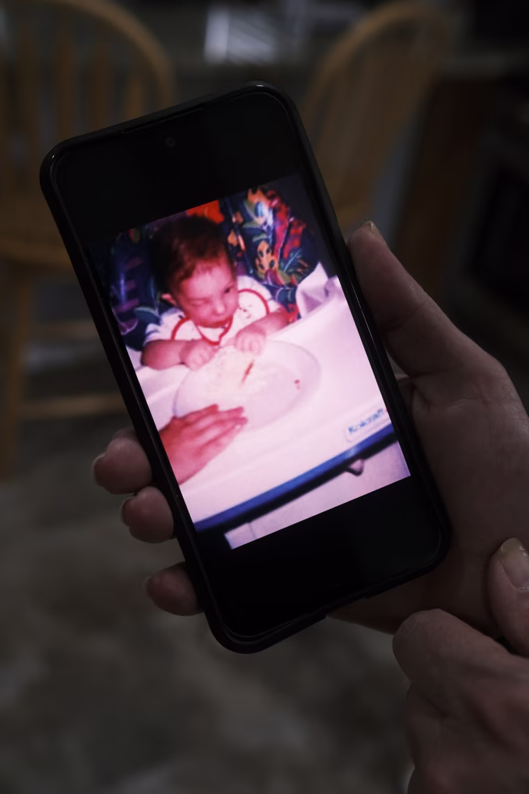 A hand holds up a cellphone displaying a photo of Jason Gonce seated in a baby chair as a baby