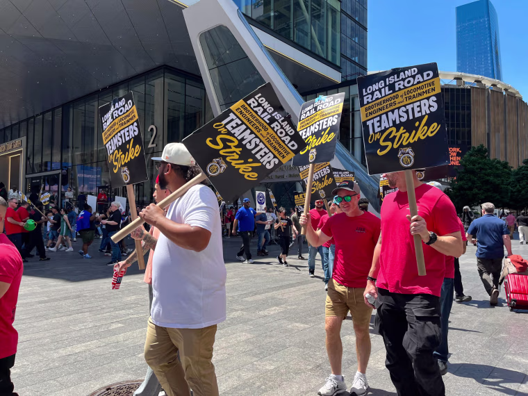 People hold picket signs proclaiming a strike while marching on the street outside