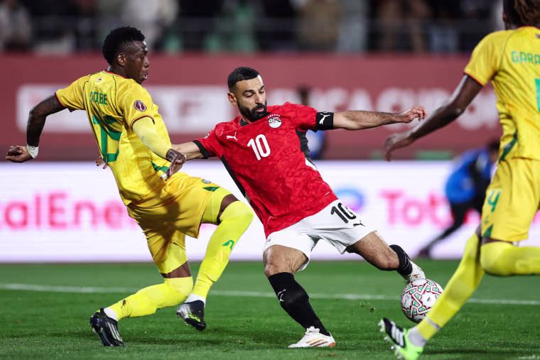 Mo Salah, center, kicks the soccer ball while in between two players from the opposing team