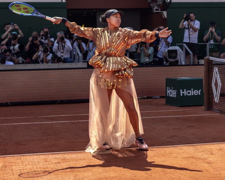 Naomi Osaka on a clay tennis court wearing a sequined outfit.