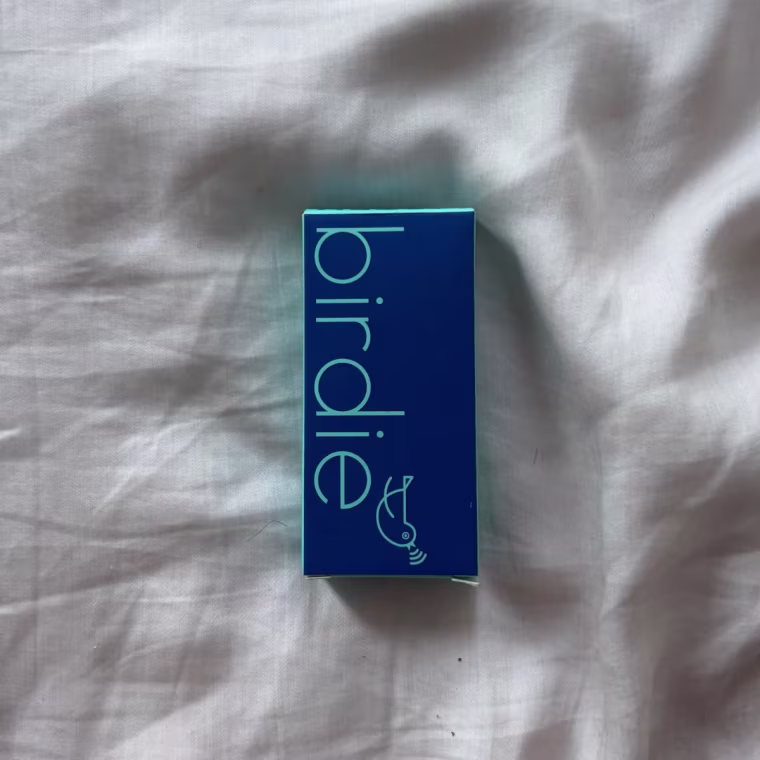 Photo of the Birdie Keychain packaging on a white bedsheet.