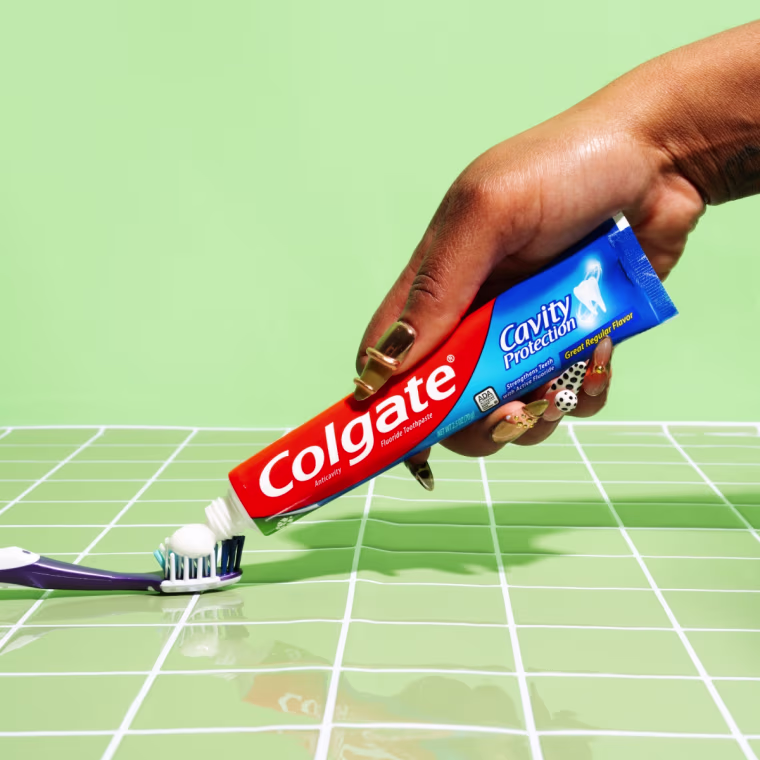 Photo of a hand squeezing Colgate’s Cavity Protection Fluoride Toothpaste onto a toothbrush