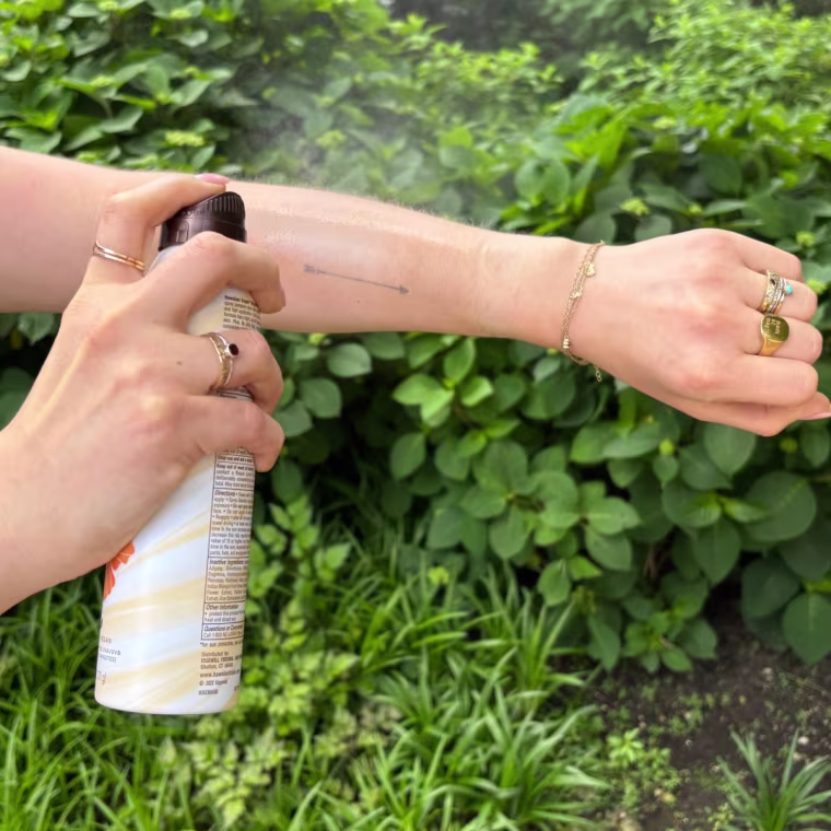 A woman applying Hawaiian Tropic’s Weightless Hydration Clear Spray Sunscreen SPF 30.