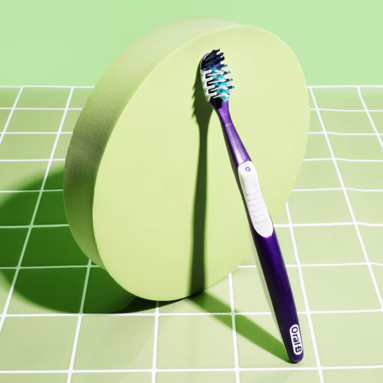 An Oral-B manual toothbrush sitting against a block with a tiled, green background.