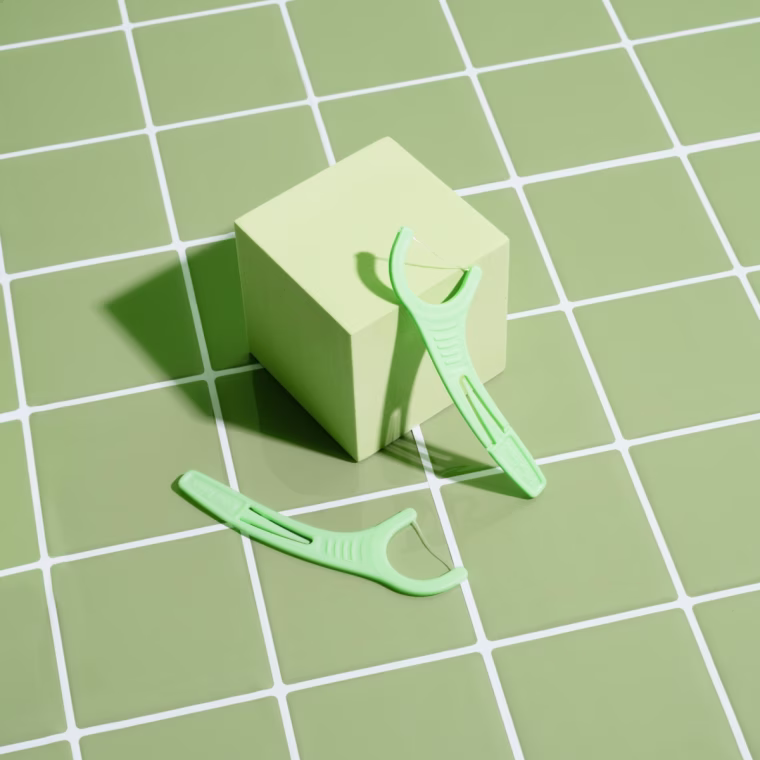 Two singular Plackers dental floss picks on a green bathroom tile background.