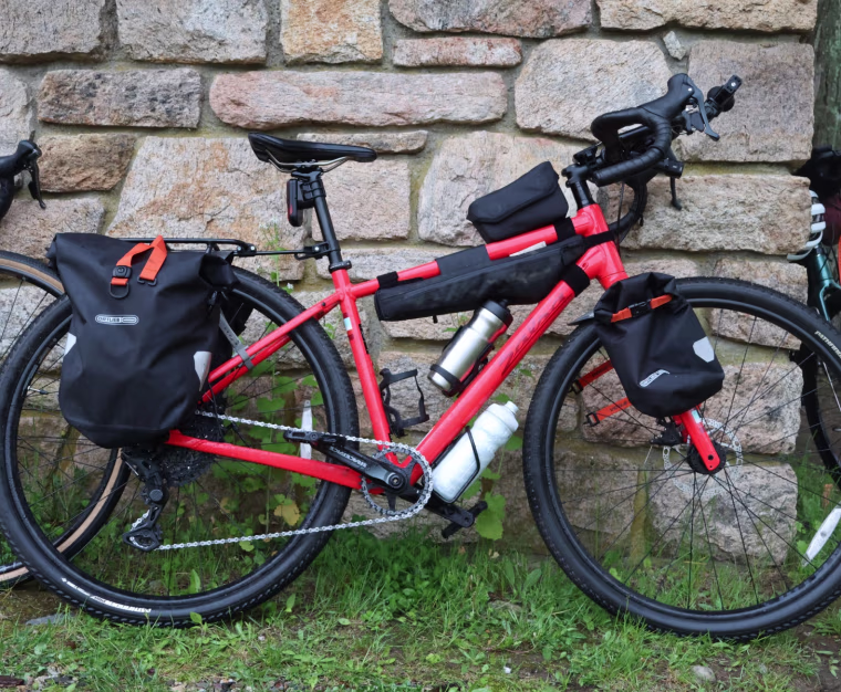 A red bike with bags attached, leaning against a stone wall.