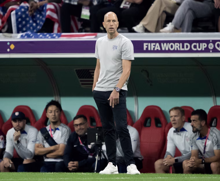 Gregg Berhalter standing on the sidelines of a soccer field.