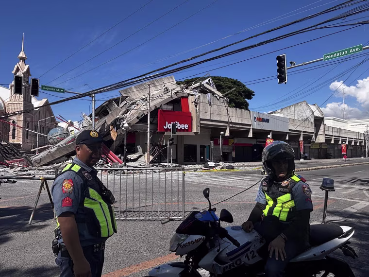 A severely damaged commercial building behind two police officers.