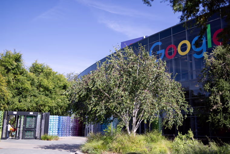 An exterior view of Google's headquarters, many trees outside of a building with all glass windows