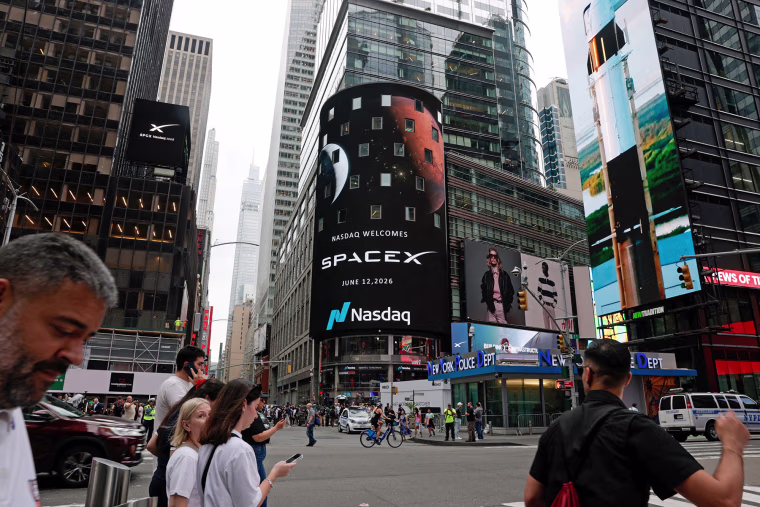 People walk near a billboard of SpaxeX on the day of SpaceX's initial public offering at the Nasdaq MarketSite in New York  on June 12, 2026.
