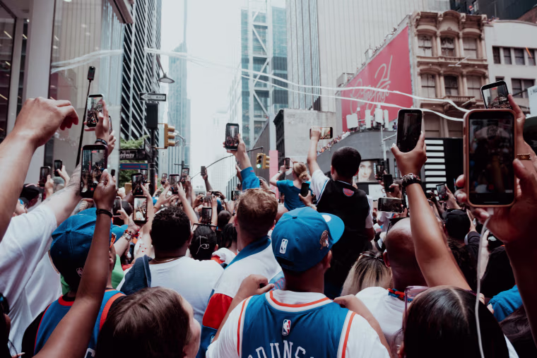 People hold their phones up to improve their views of the parade floats on Maiden Lane and Broadway.