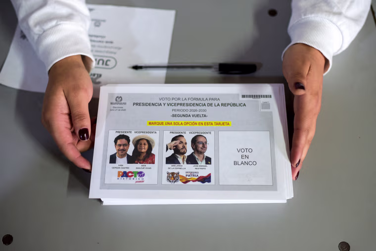 A worker holds electoral material on a table showing Colombian presidential candidates Iván Cepeda and Abelardo de la Espriella