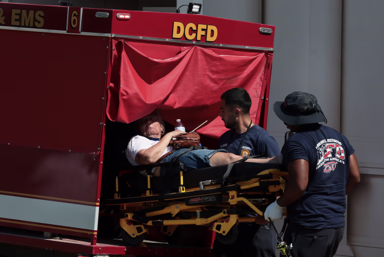 Two paramedics lifting a person on a stretcher into a red emergency vehicle.