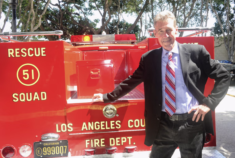 Randolph Mantooth rests one hand on a vintage red fire engine.
