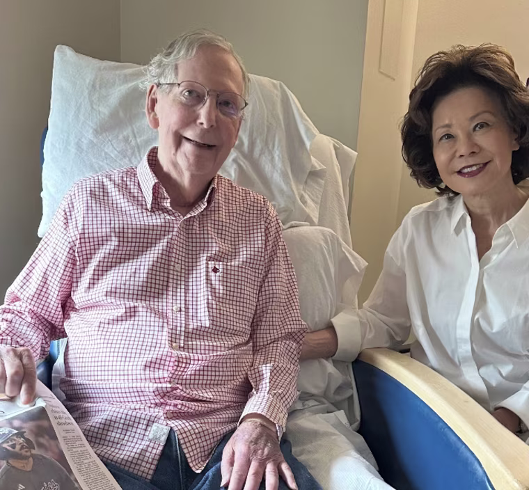 Mitch McConnell smiling with his wife while seated against a stack of white pillows.