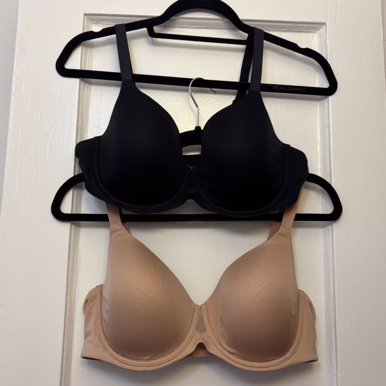 Two Thirdlove TempSync T-Shirt Bras on black hangers, one on top of the other: top (black) and bottom (nude)