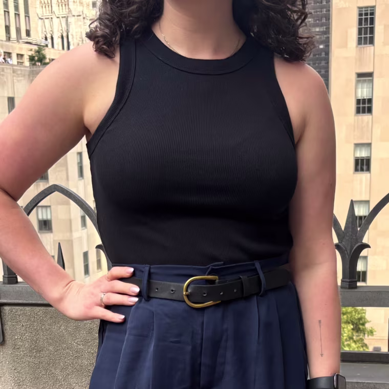 A woman standing outside and wearing a black tank top.