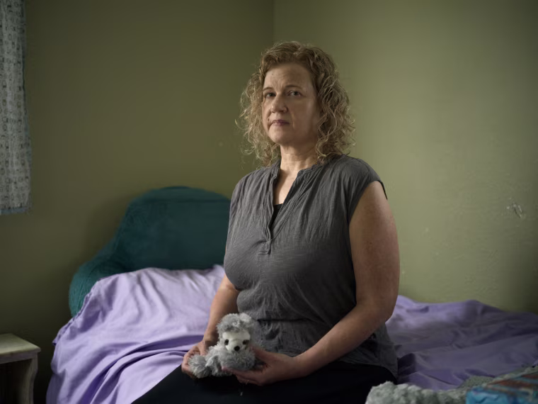 Elyse Thorpe sits on May's bed holding a stuffed animal loved by May.