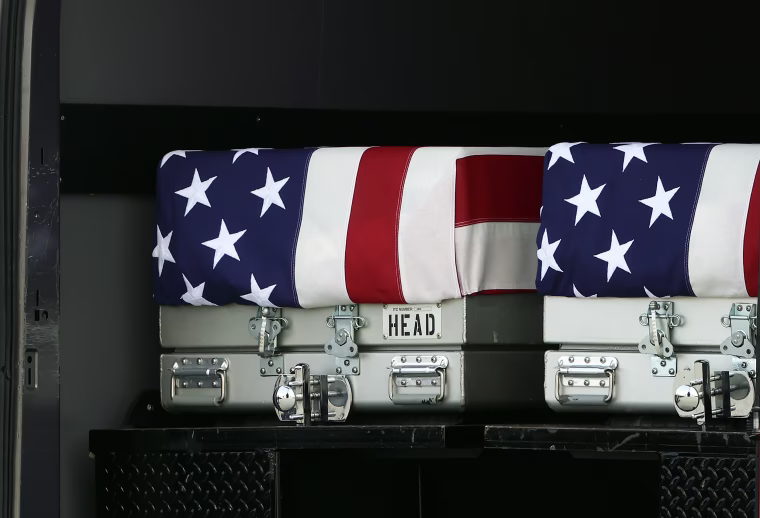 Two metal coffins with American flags draped over them in the back of a cargo truck.