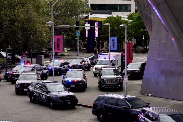 A dozen law enforcement vehicles with lights flashing parked outside an event center in downtown Seattle.