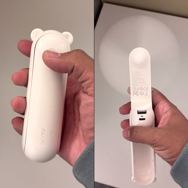 Person holding white Jisulife handheld fan in their right hand.