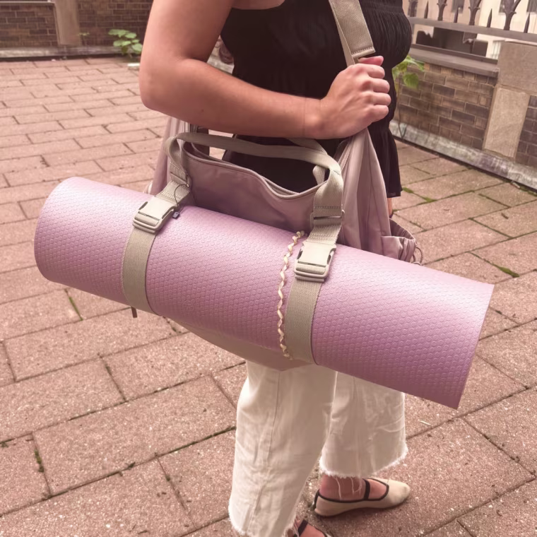 Woman holding Calpak gym duffel with a rolled up yoga mat attached to it.