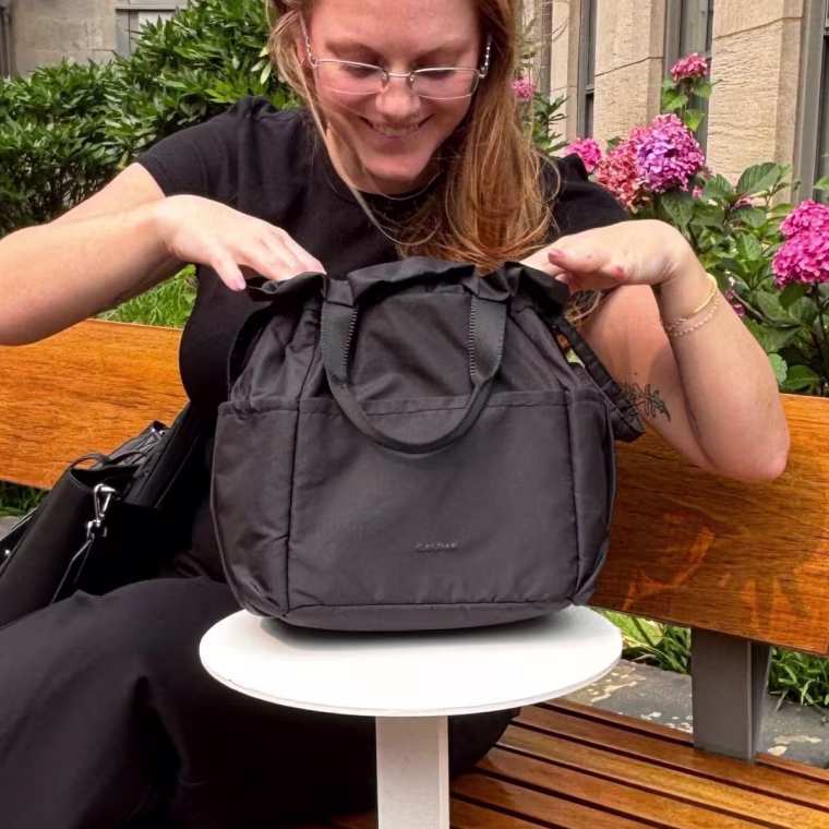Woman sitting with Calpak Insulated Lunch Bag next to her.