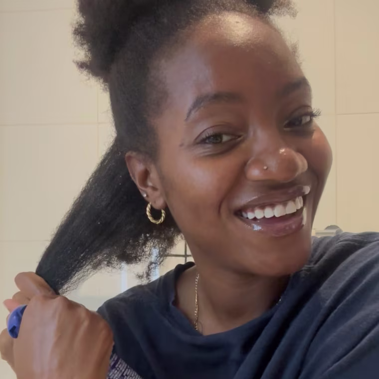 Spraying the Cecred Detangling Spray onto stretched hair while standing in a bathroom.