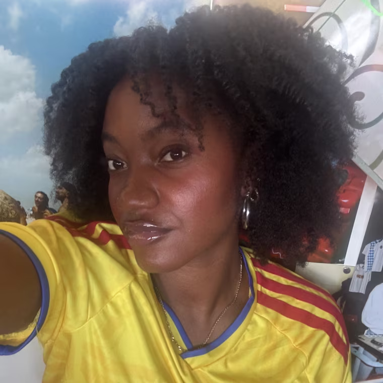 A selfie of Morris with a blown-out braidout using the Cecred Thermal Shield Mist, wearing a yellow soccer jersey in front of a wall of graffiti art.