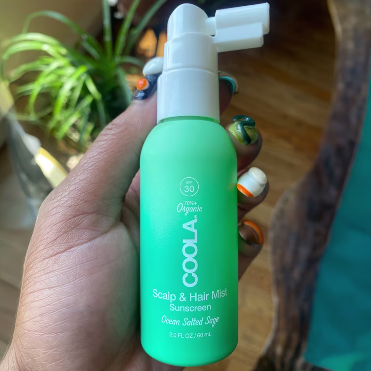 Woman holding bottle of Coola hair and scalp sunscreen