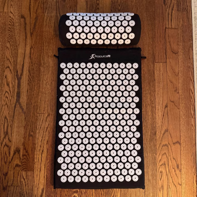 ProsourceFit’s Acupressure Mat and Pillow Set on a wood floor.