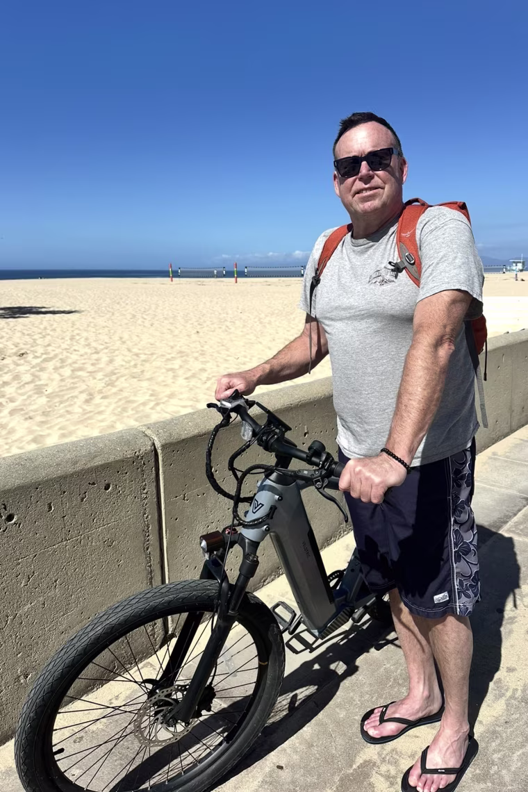 Christopher Claunch posing for a photo on the beach while holding his bike.