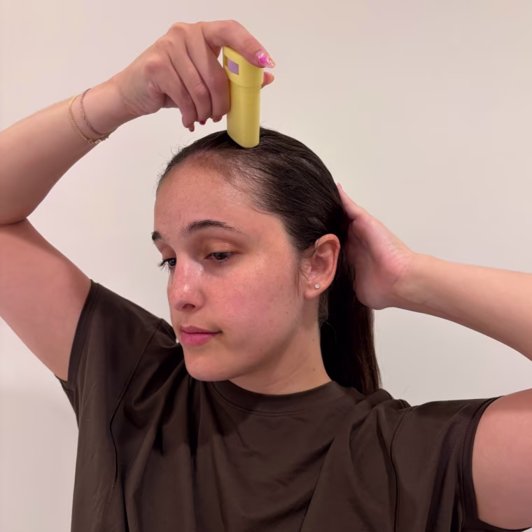 Woman applying JVN wax stick to side of her hair