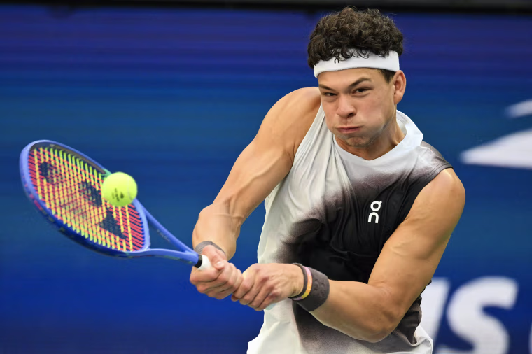 Ben Shelton swings his tennis racket with both hands.