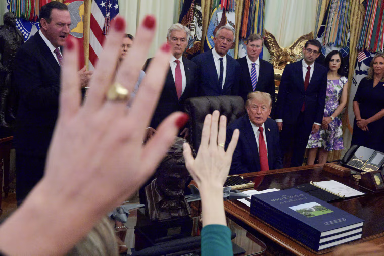President Trump speaks to reporters while seated at his desk in the Oval Office and flanked by cabinet members.