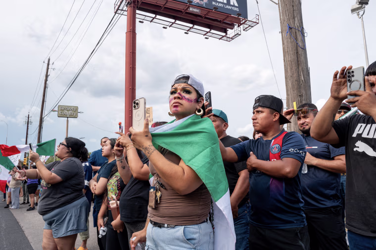 People holding cell phones and standing alongside a road during a demonstration.