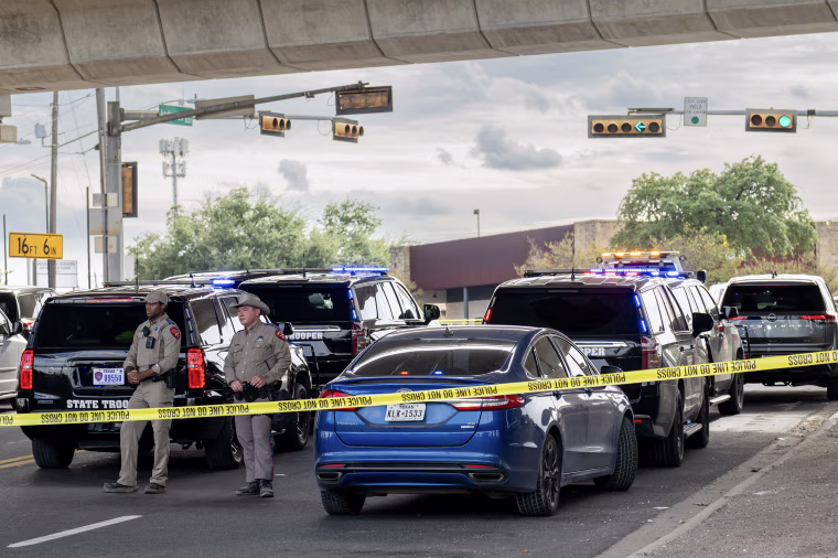 Two law enforcement agents standing behind police tape under an overpass.