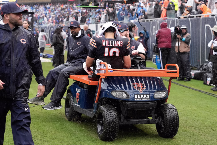 Caleb Williams rides in a golf cart on the sidelines, facing away from the camera.