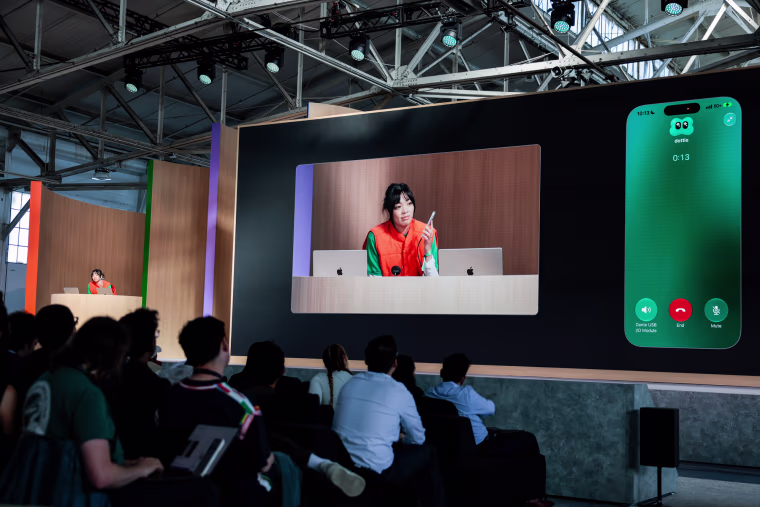 Holly Li does an on stage demonstration of the AI assistant using a phone that is enlarged on a screen next to her on stage
