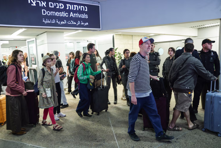 Passengers with suitcases walk into the domestic arrivals section of an airport