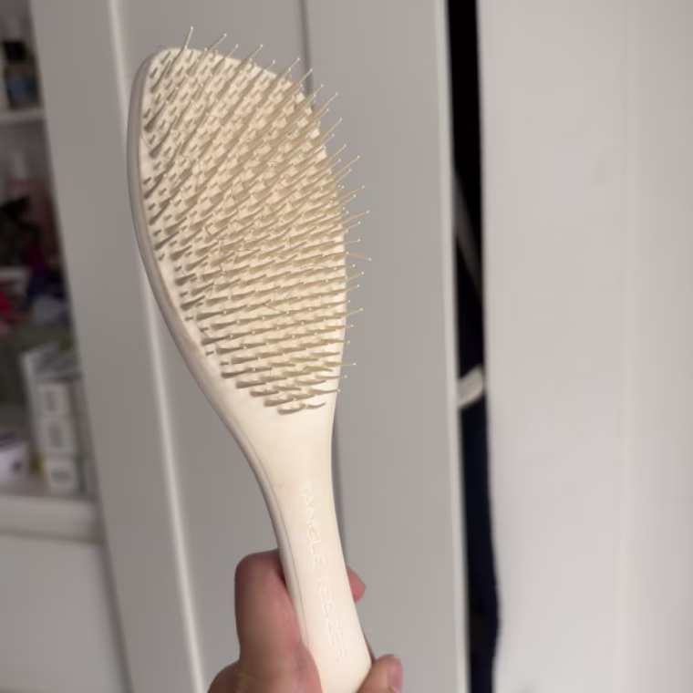 Holding up the Tangle Teezer The Complete Carebrush for Straight to Wavy Hair in front of a white closet door.