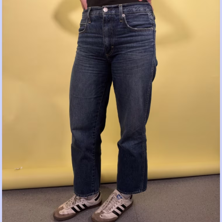 Woman wearing the AMO Denim Billie Metaphor Jeans in front of a yellow backdrop.