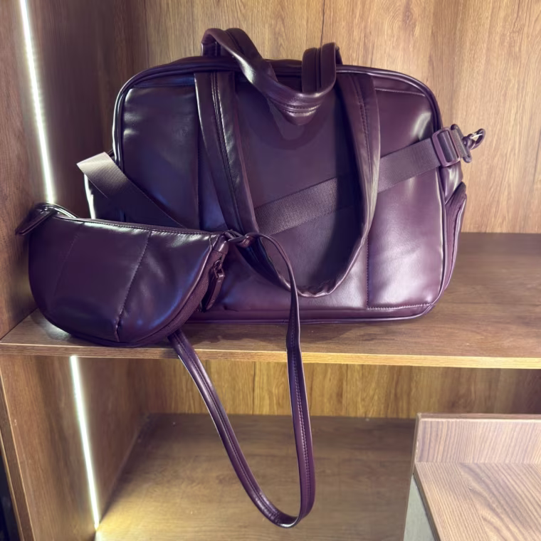 Photo of a dark purple duffel sitting on a shelf with a smaller version looped around it
